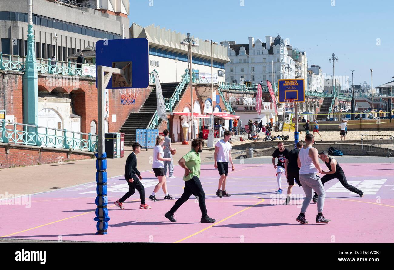 Brighton UK 29th March 2021 - Basketball players enjoy playing on the reopened Brighton seafront court on a lovely sunny day as lockdown restrictions have started to ease in England  Temperatures are expected to reach the mid 20s in some parts of the South East over next few days. : Credit Simon Dack / Alamy Live News Stock Photo