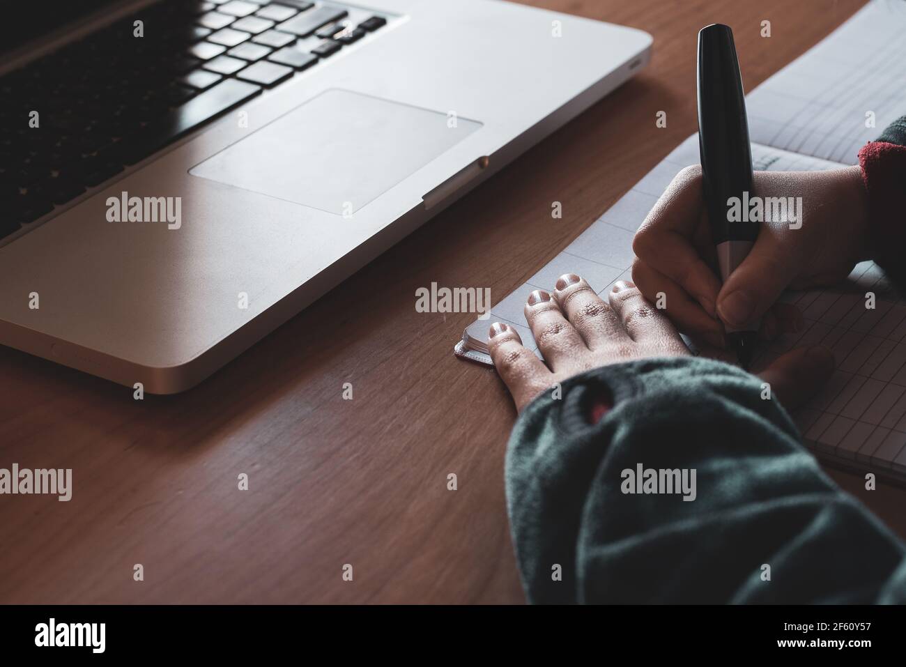 Hands of a boy writing on a notebook and laptop. Homework concept. Stock Photo