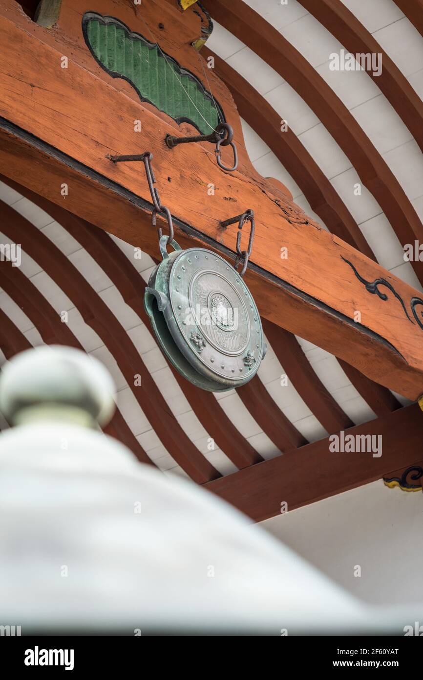 A bronze metal flat bell gong hanging in an orange white building in
