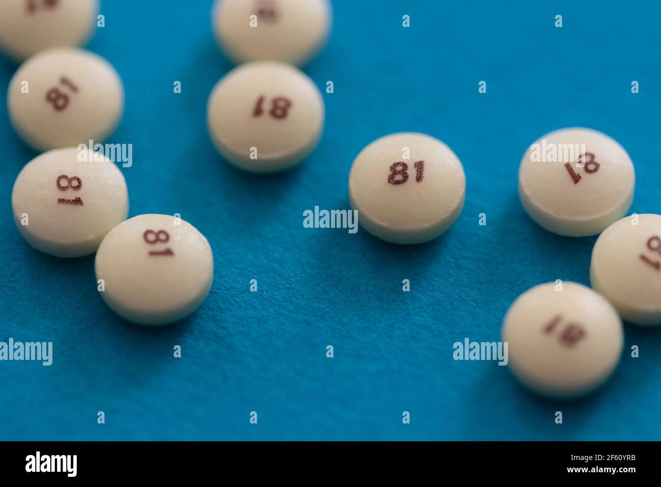 scattered low dose 81 milligrams aspirin on a turquoise blue background with a low depth of field, commonly used as a preventive medicine for heart di Stock Photo