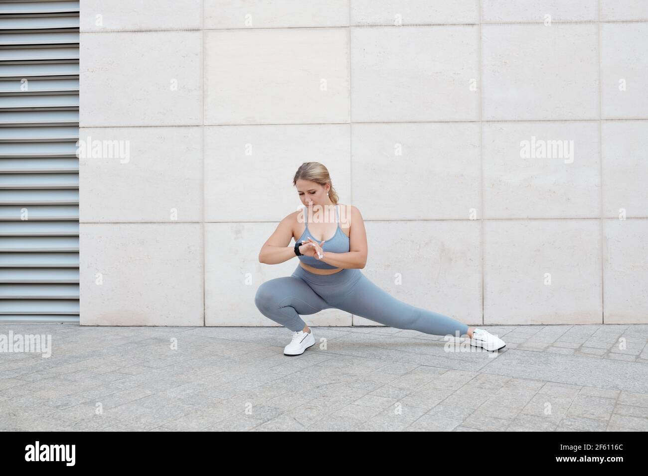 Fit young plus size woman doing lunges and checking fitness treker on her wrist when training outdoors Stock Photo