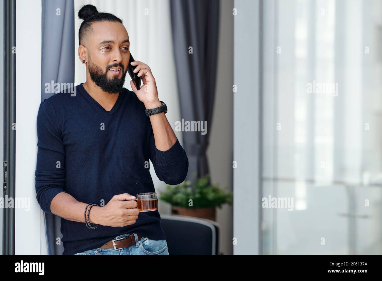 Portrait of positive bearded man drinking morning coffee and talking on phone with colleague or employee Stock Photo