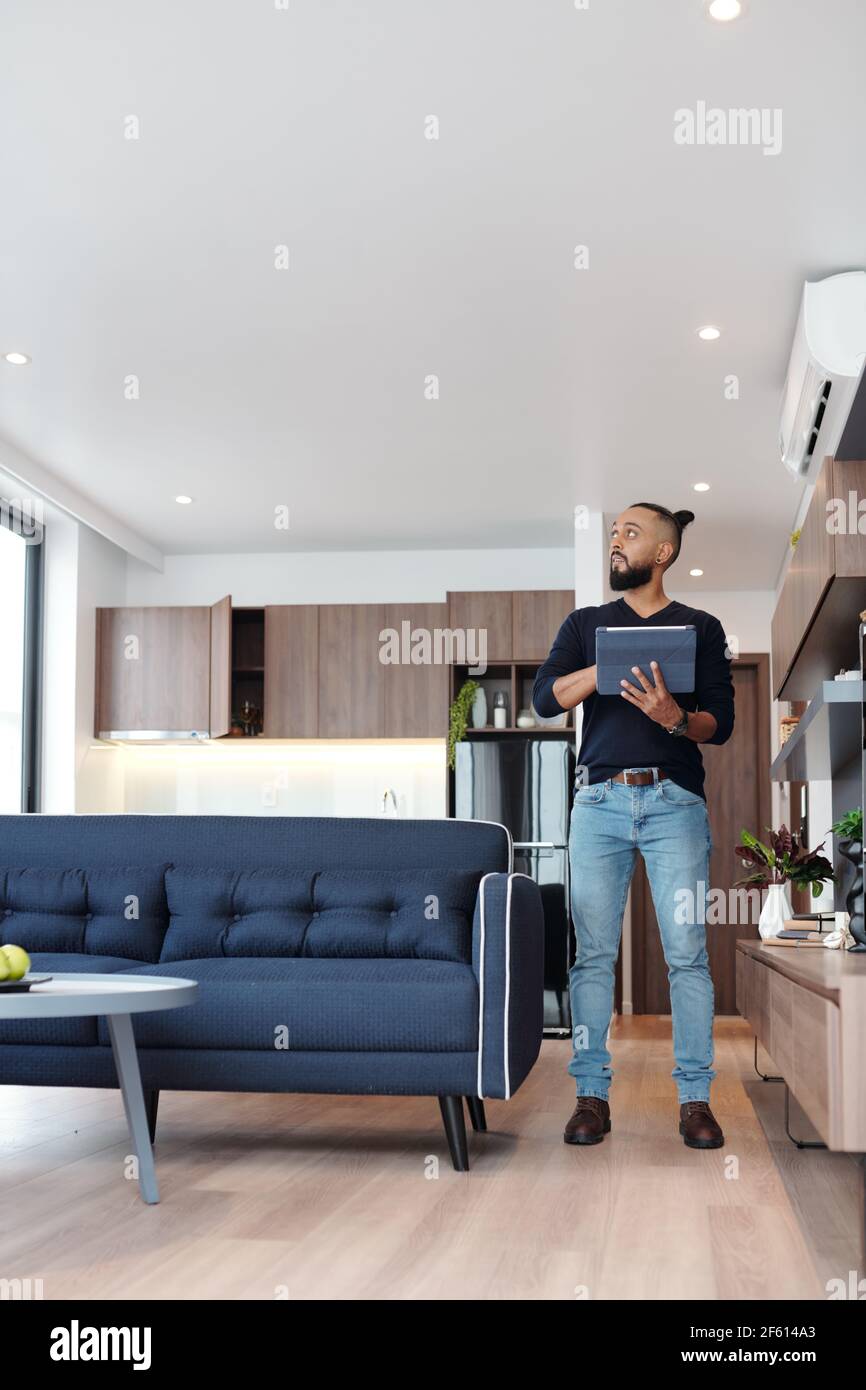 Handsome bearded man using application on tablet computer to control temperature and light in his studio apartment Stock Photo