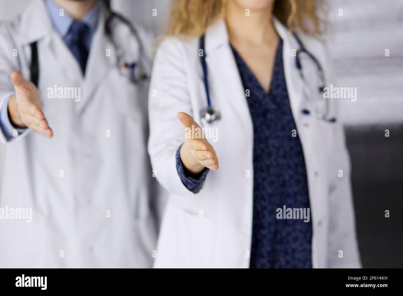 Two doctors standing and offering helping hand for shaking hand or