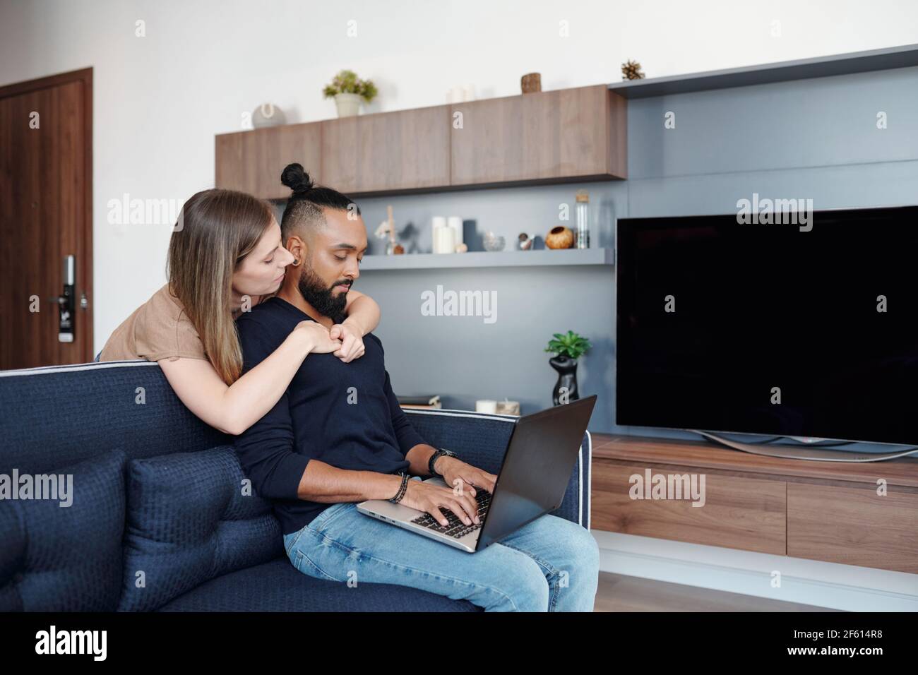 Pretty young woman hugging her boyfriend from behind when he is working ...