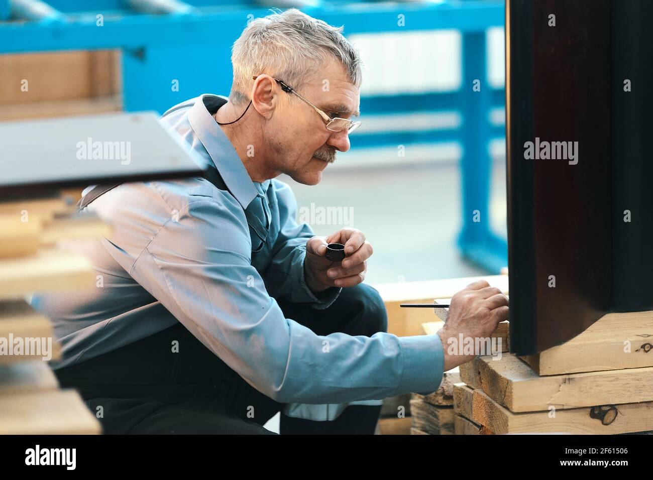 An elderly worker carefully restores furniture in a carpenter's workshop during the day. Stock Photo