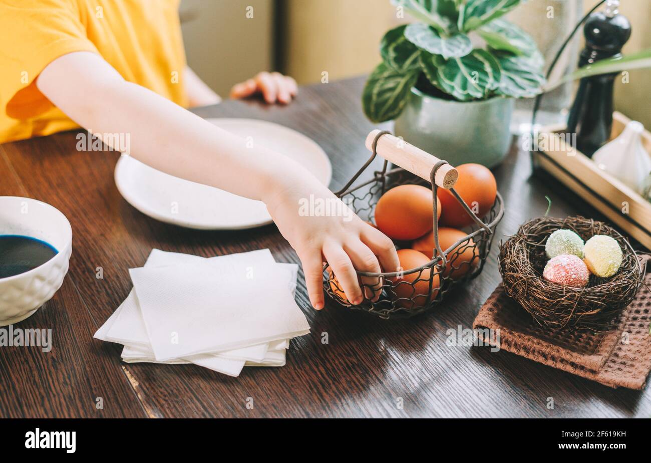 Easter day. Kid boy painting eggs on wooden background. Child sitting in a kitchen. Preparing for Easter, creative homemade decoration Stock Photo