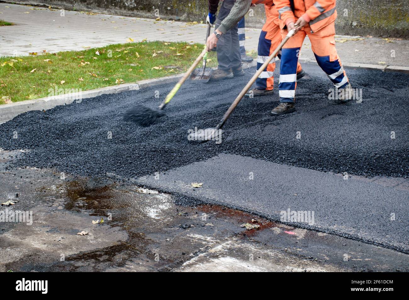 Paving workers move very fast their shovels while adjusting new layer of asphalt in reconstruction of road. Stock Photo