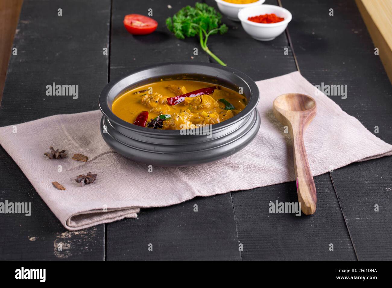 Chicken with raw banana curry (plantain),spicy chicken with green banana tastier indian dish arranged in a tableware which is on a tissue with black b Stock Photo