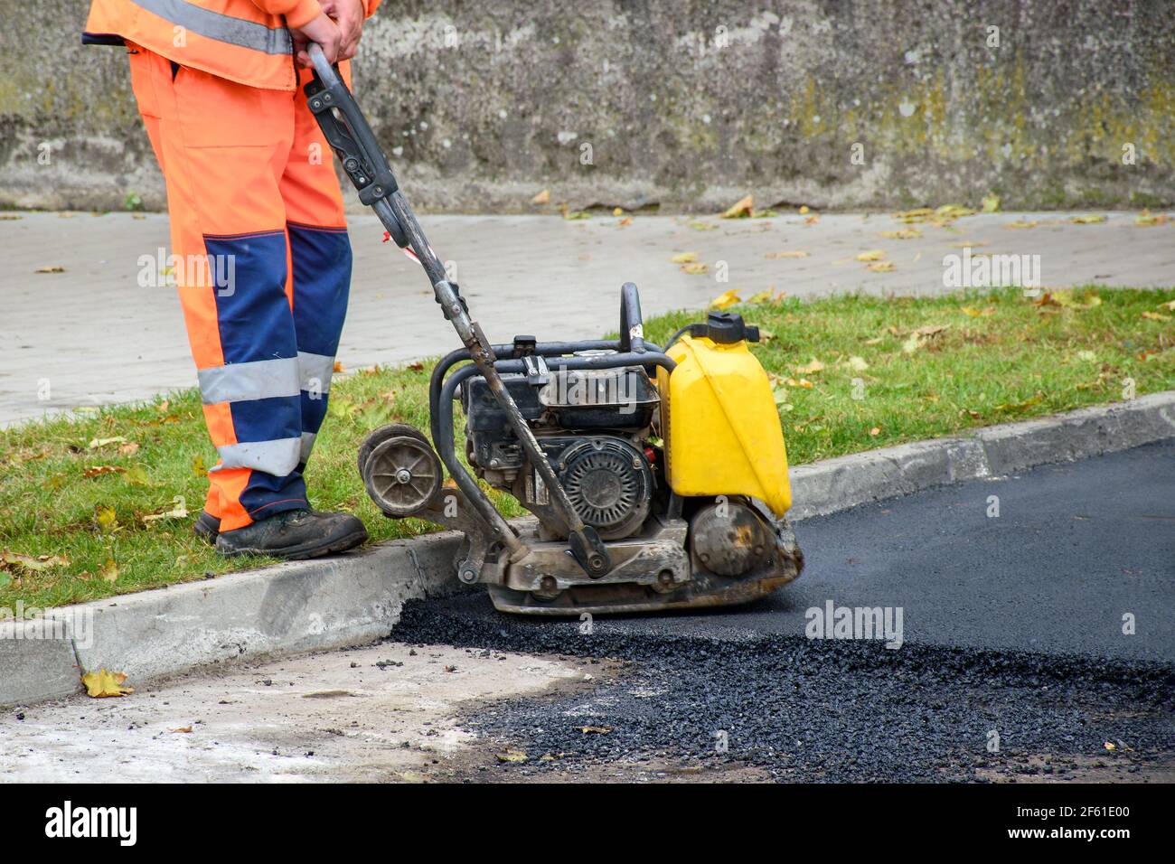 Paving worker uses vibratory plate compactor to compact new asphalt near curbstones Stock Photo