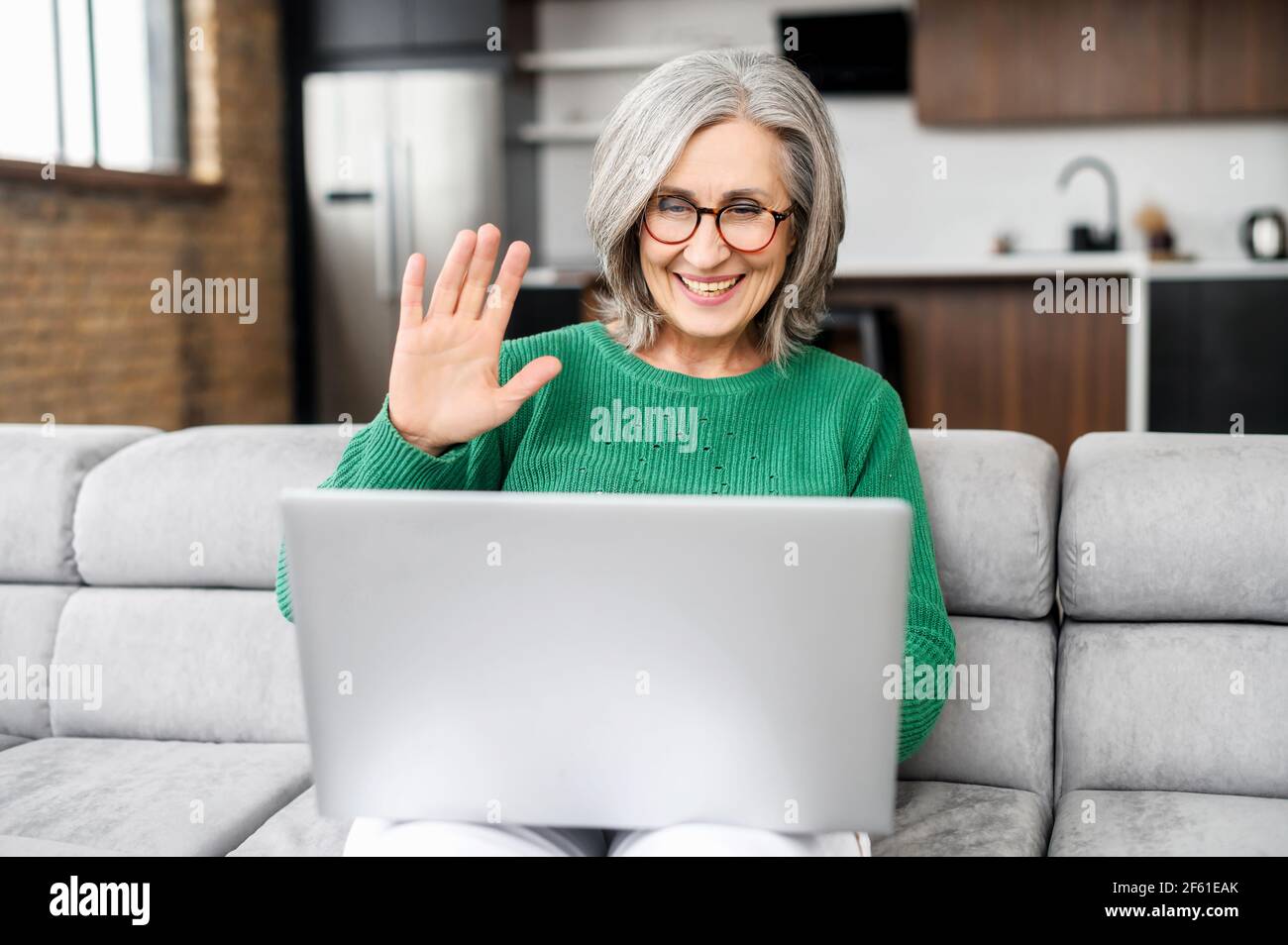 Modern mature woman in touch with a family, friends or colleagues via video connect. Senior female using laptop computer for video call, smiling and waving hello into webcam, video conference remotely Stock Photo