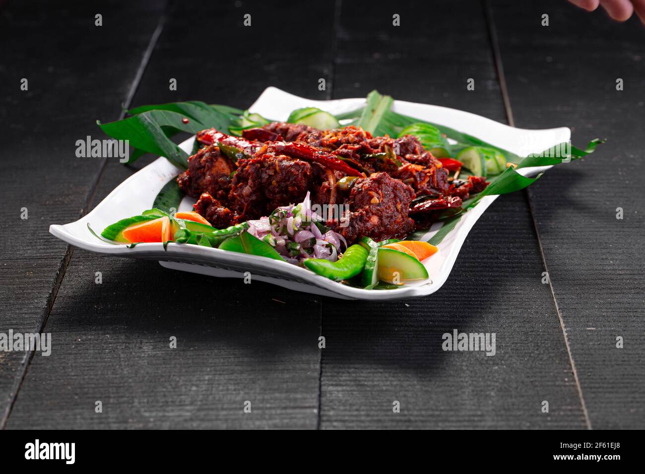 Chicken peralan or chicken dry curry, kerala special chicken dish which is beautifully arranged in a white tableware lined with banana leaf Stock Photo
