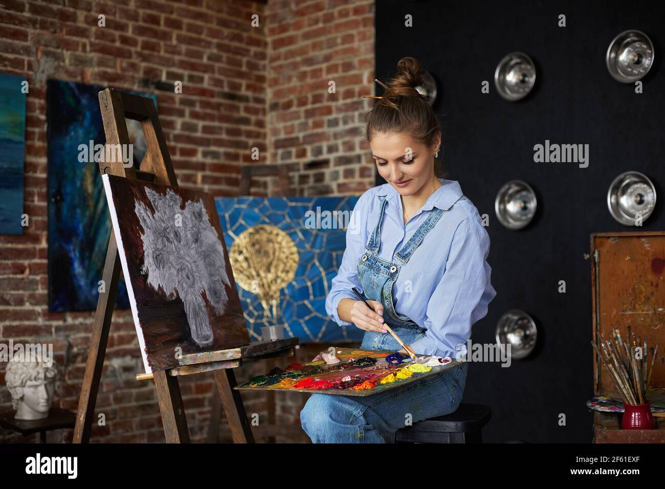 Young beautiful female artist painting still life with sunflower on ...