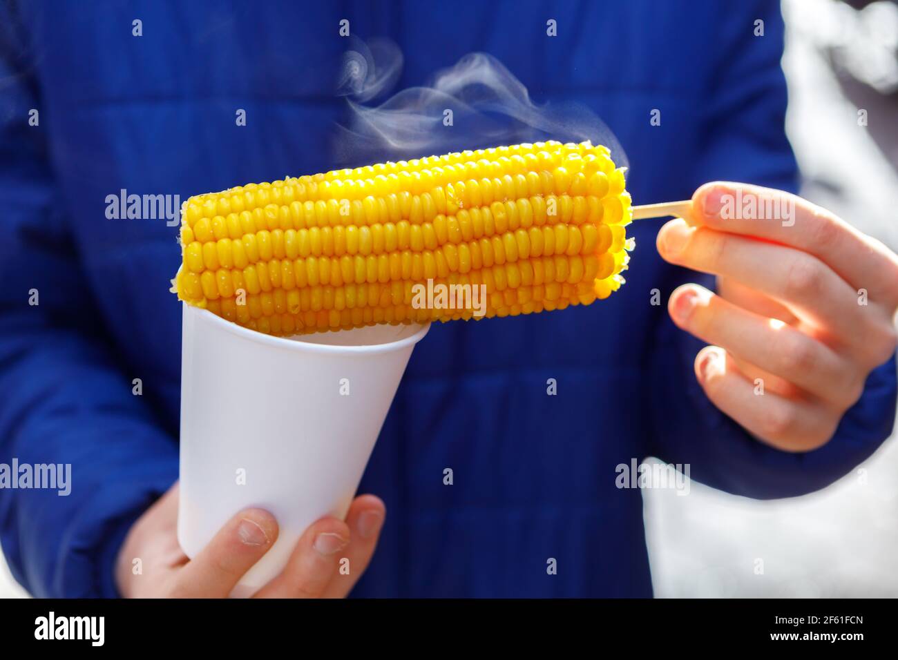 An ear of freshly boiled corn in his hands. Steam comes from the cob. Fast food concept. Stock Photo