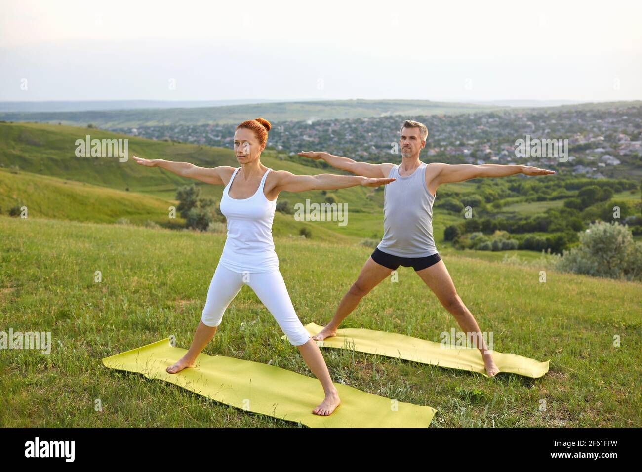 Middle aged couple doing Five Pointed Star asana while practicing yoga together on grassy hill Stock Photo