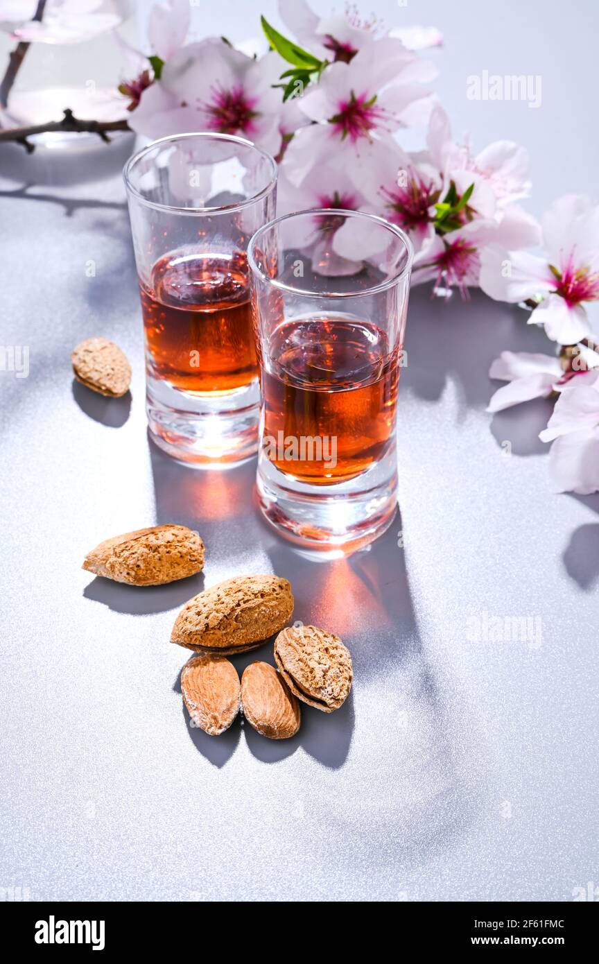 almond liquor. The traditional strong drink in italy to complete the dinner is a liqueur made from nuts and berries. Ratafia, alcohol in shot. top view on the table and blooming almonds. Copy space Stock Photo