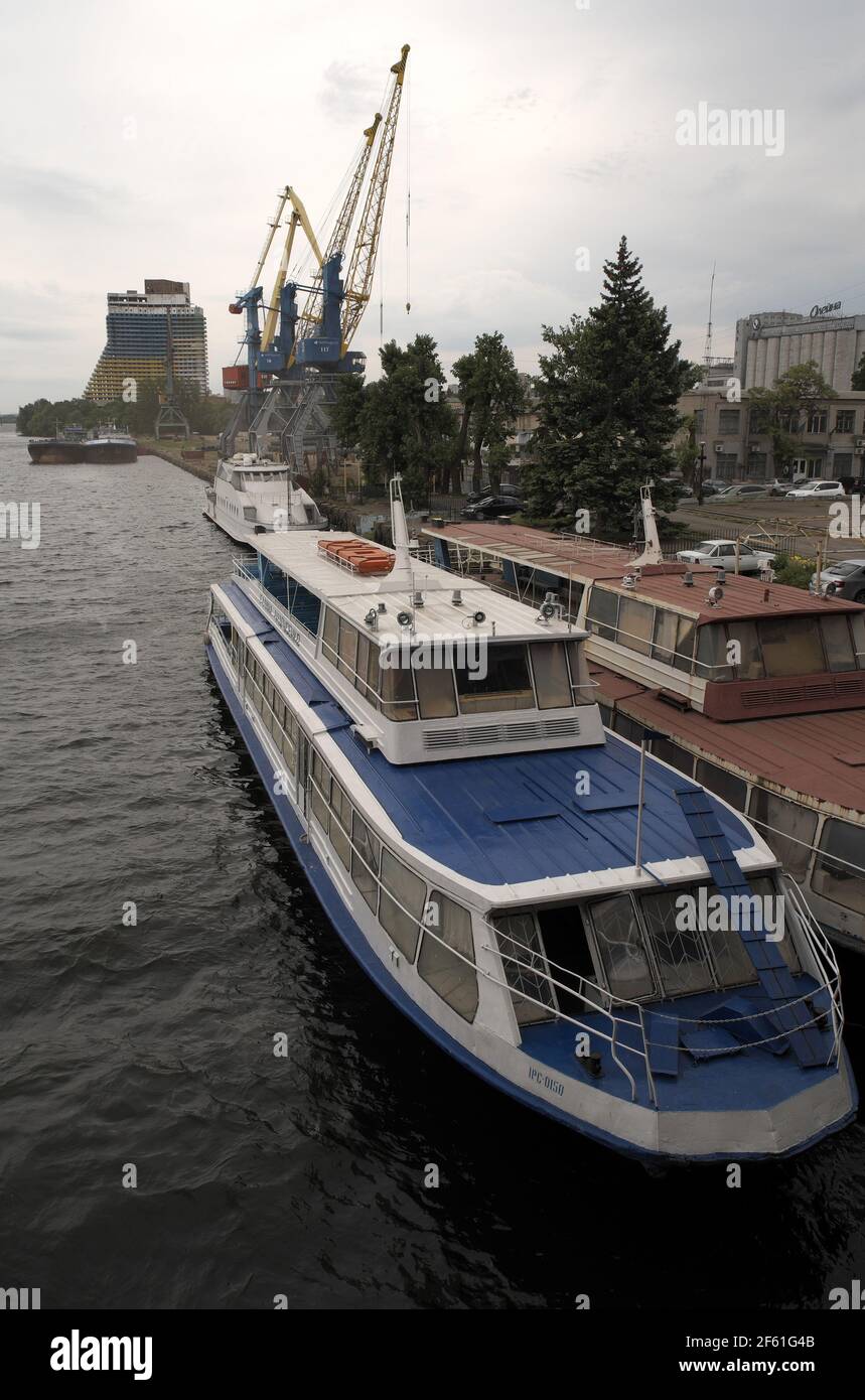 River cruise boat moored beside quayside, with cranes beyond, River Dnieper, Dnipro, Ukraine. Stock Photo