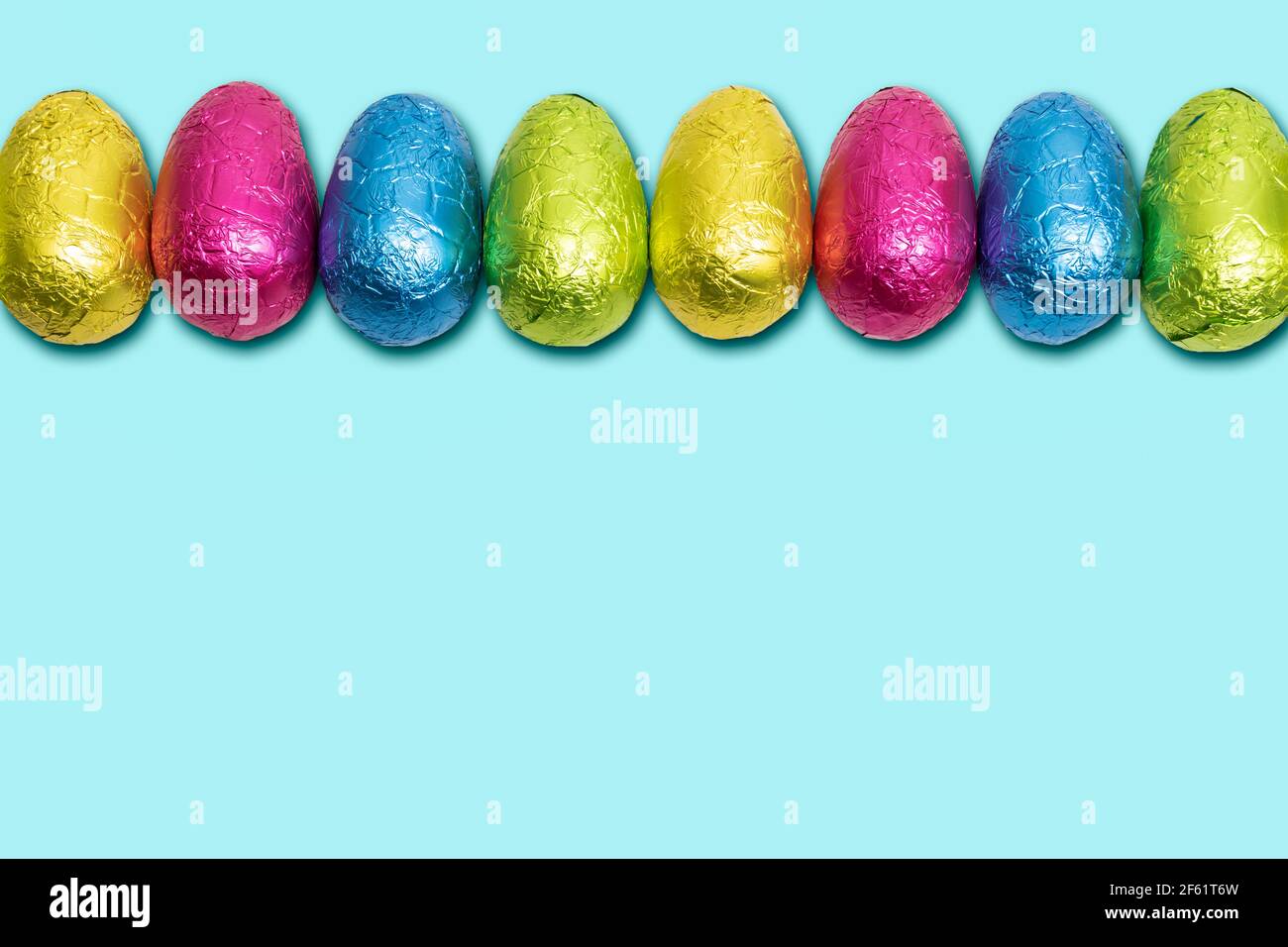 Chocolate Easter eggs wrapped in foil. Colorful Easter egg border. Stock Photo