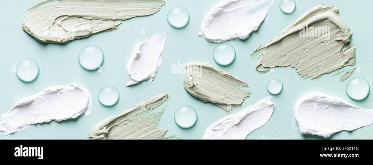 Green and white clay smears and hyaluronic acid serum drops on turquoise background. Stock Photo