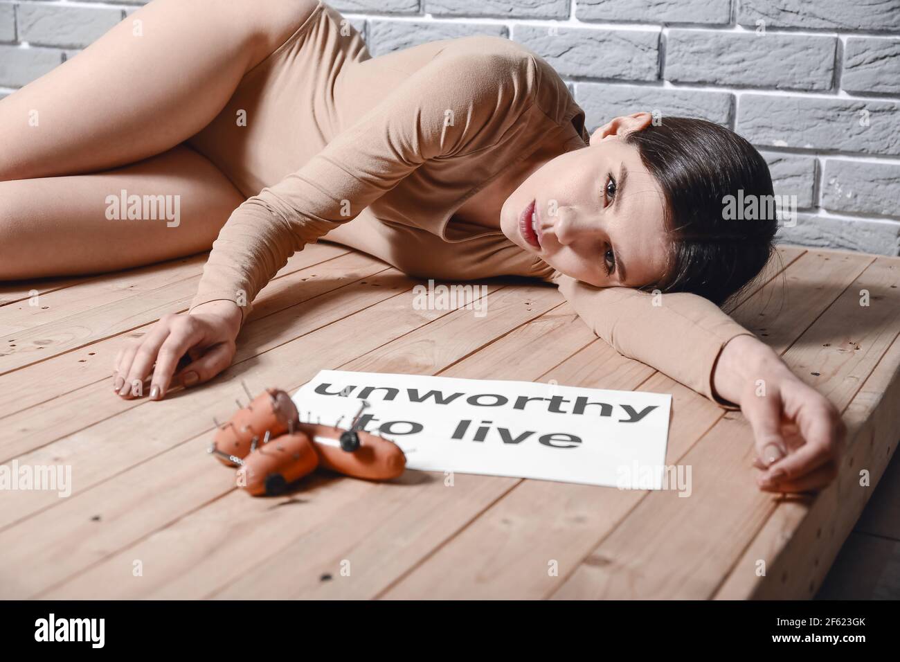 Young woman lying on floor near sausages with nails. Concept of cruelty to animals Stock Photo