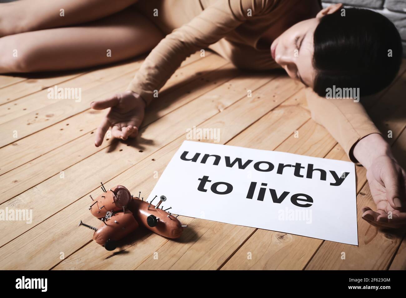 Young woman lying on floor near sausages with nails. Concept of cruelty