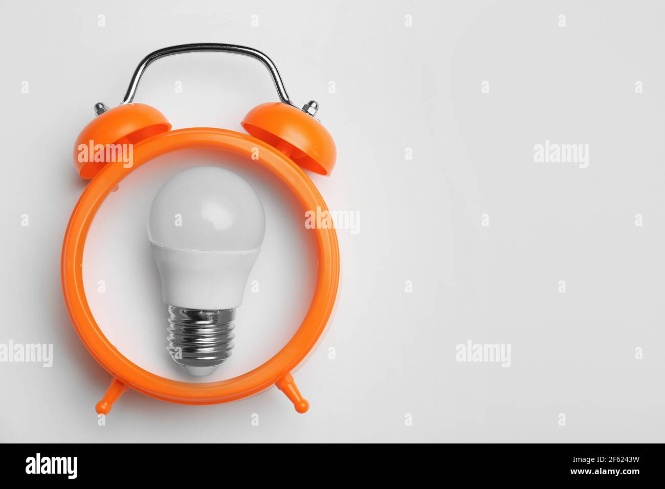 Light bulb with alarm clock on light background. Concept of business