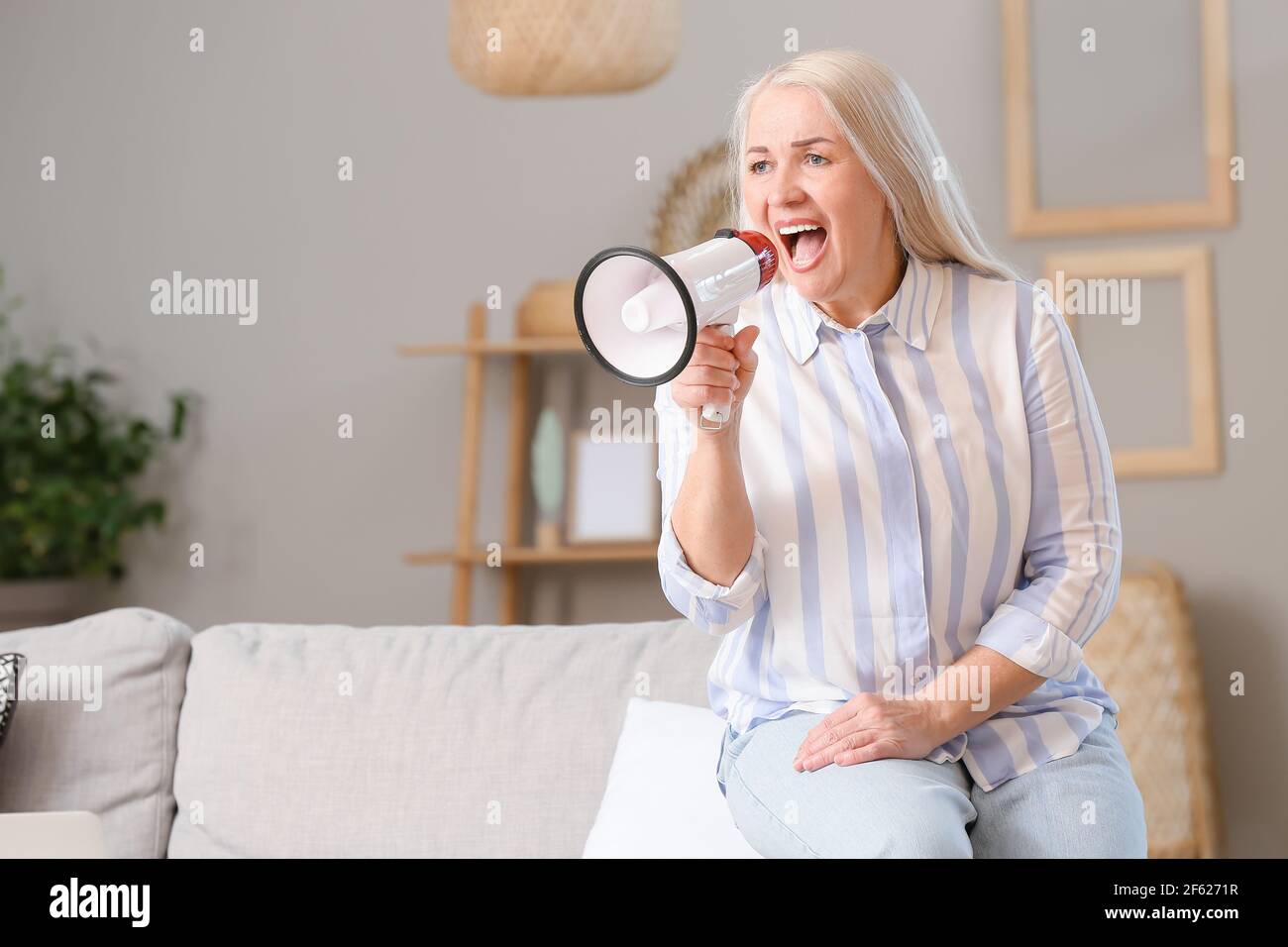 Screaming mature woman with megaphone at home Stock Photo