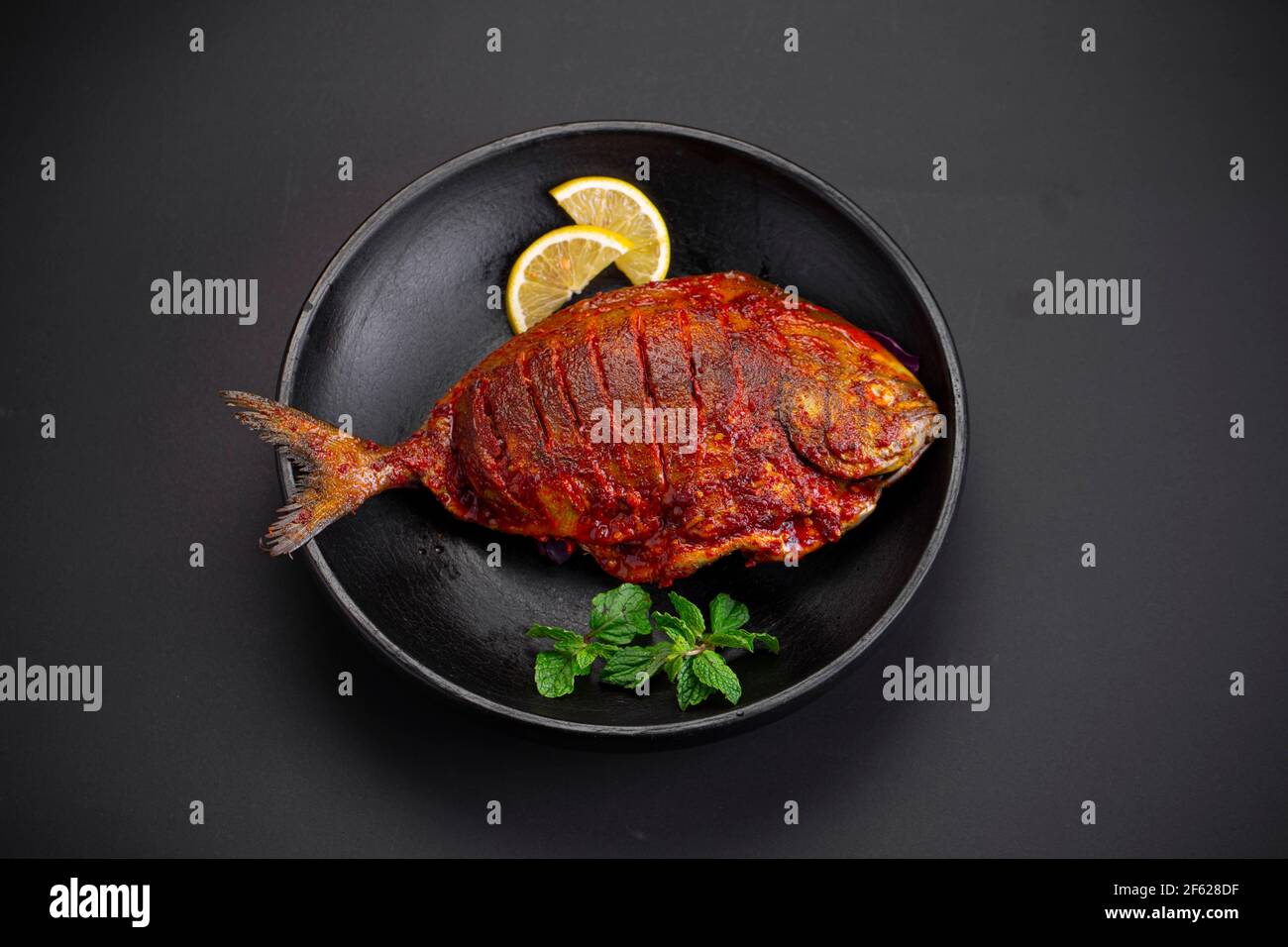 Pomfret fry arranged in  a black plate and garnished with lemon slices on black textured background. Stock Photo