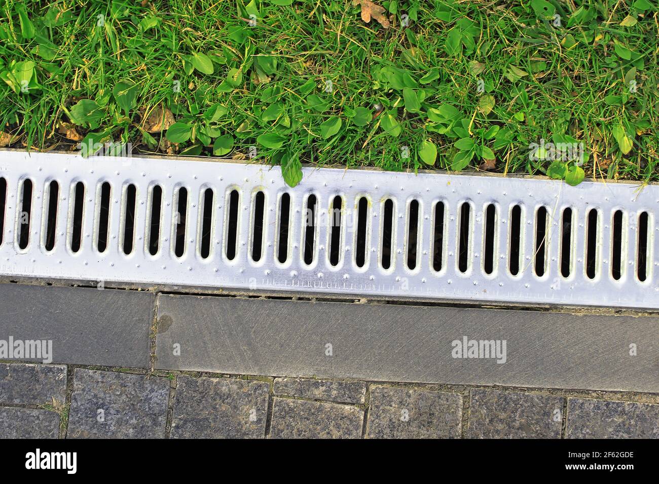 Drainage system separates the grass and the paved sidewalk. Sewerage and grate on the ground for water drainage Stock Photo