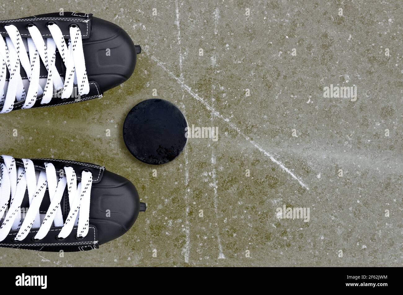 Pair of hockey skates with puck on a ice rink. Stock Photo