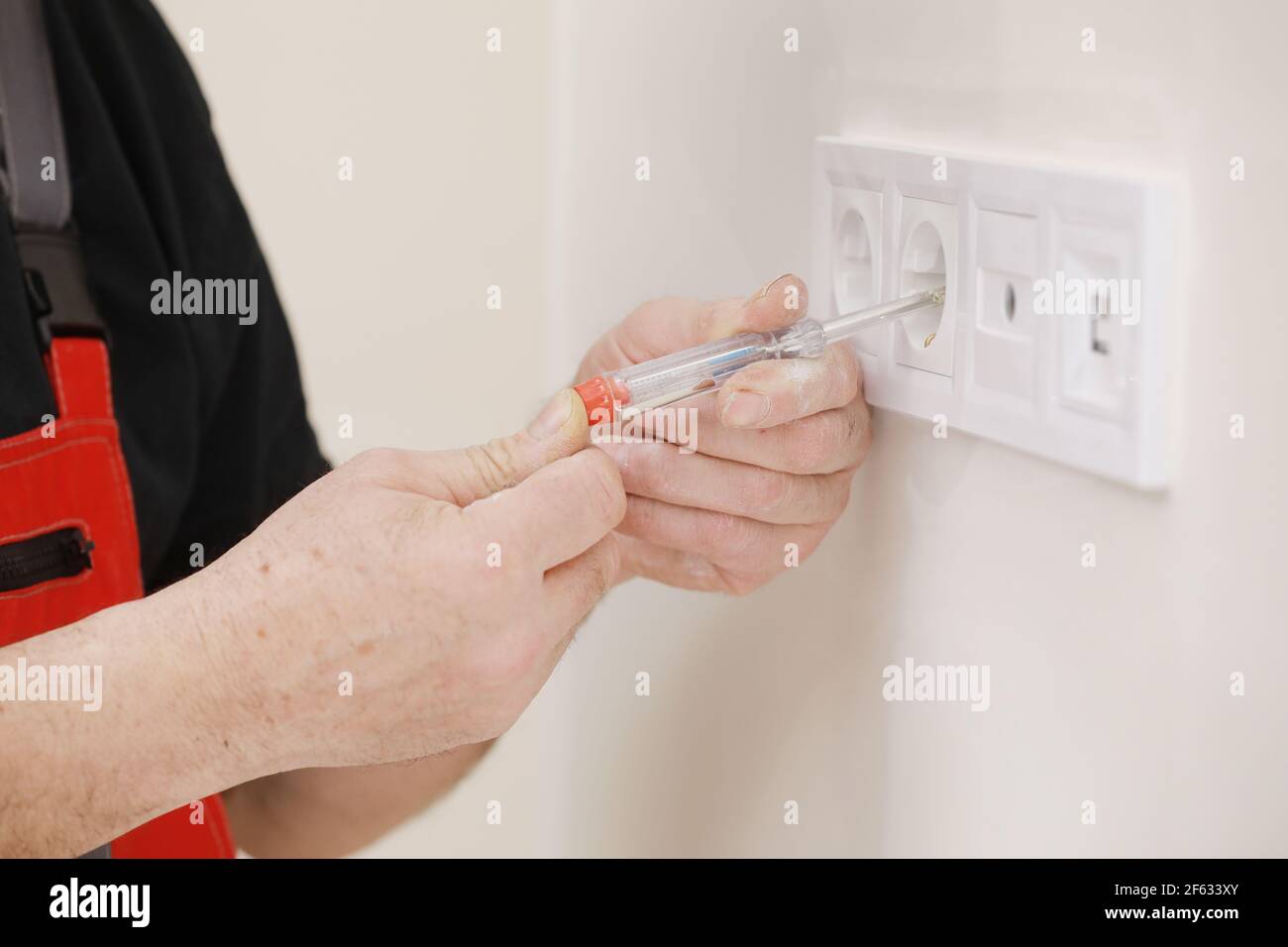 Electrician hands tighten electrical wires in wall fixture or socket