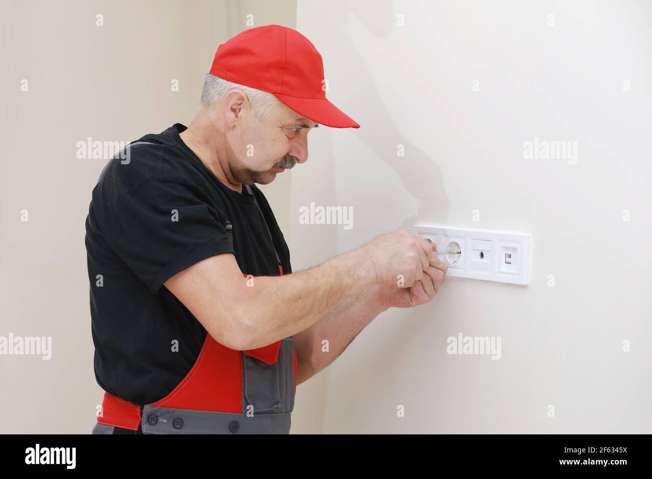 Electrician hands tighten electrical wires in wall fixture or socket