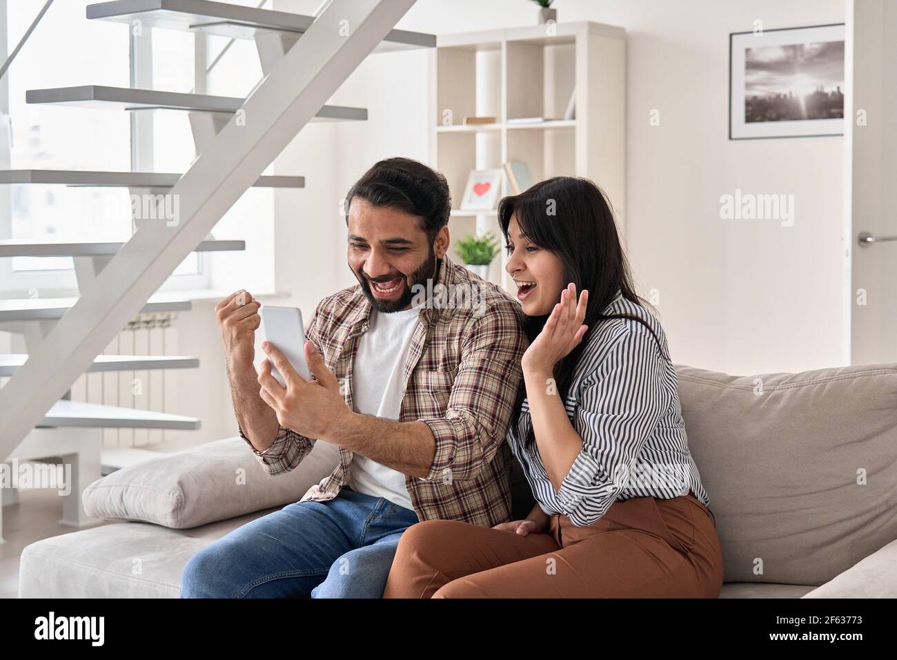 Excited happy young indian couple winners look at smart phone celebrate win. Stock Photo