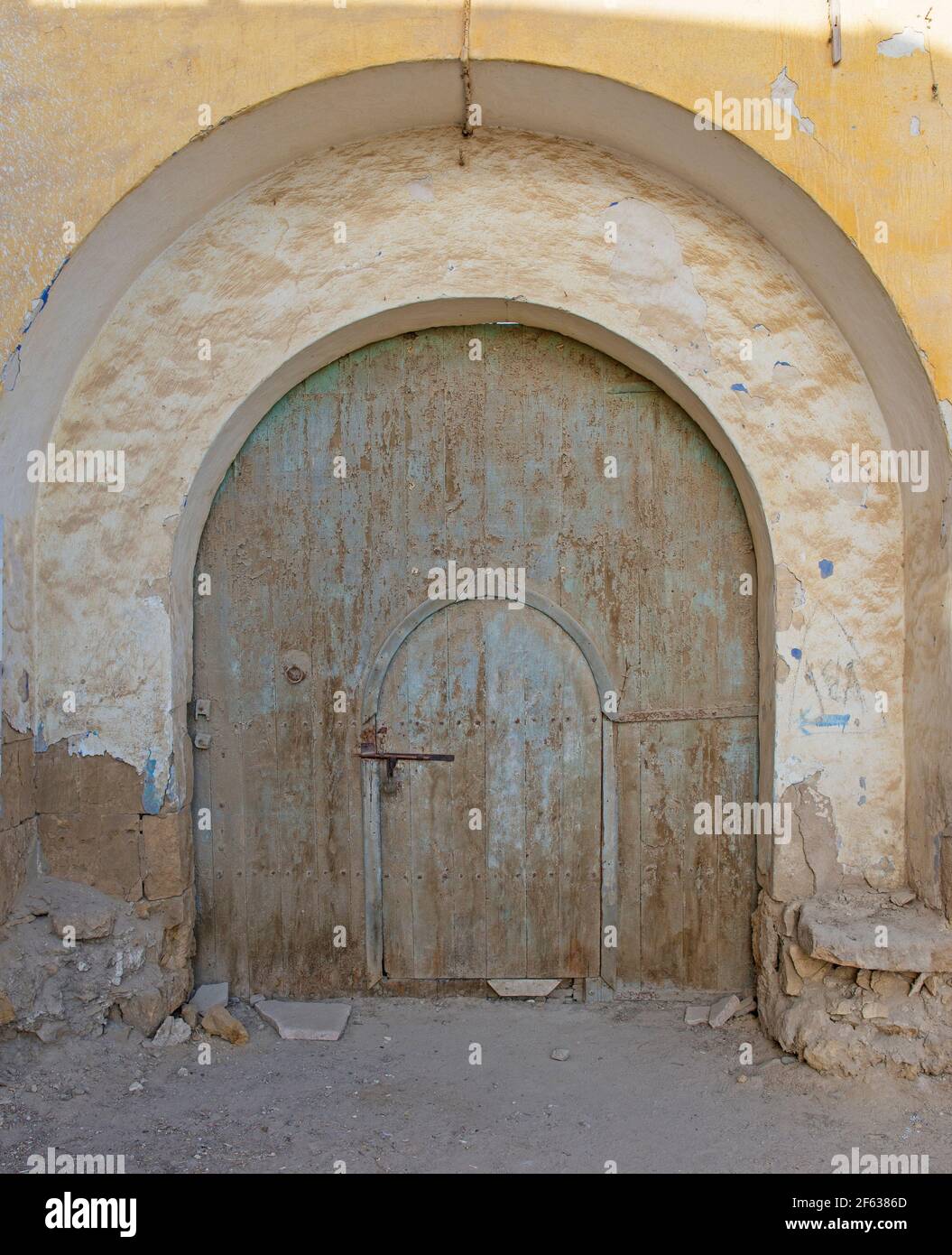 Old rustic wooden arched door in wall of abandoned traditional egyptian house Stock Photo