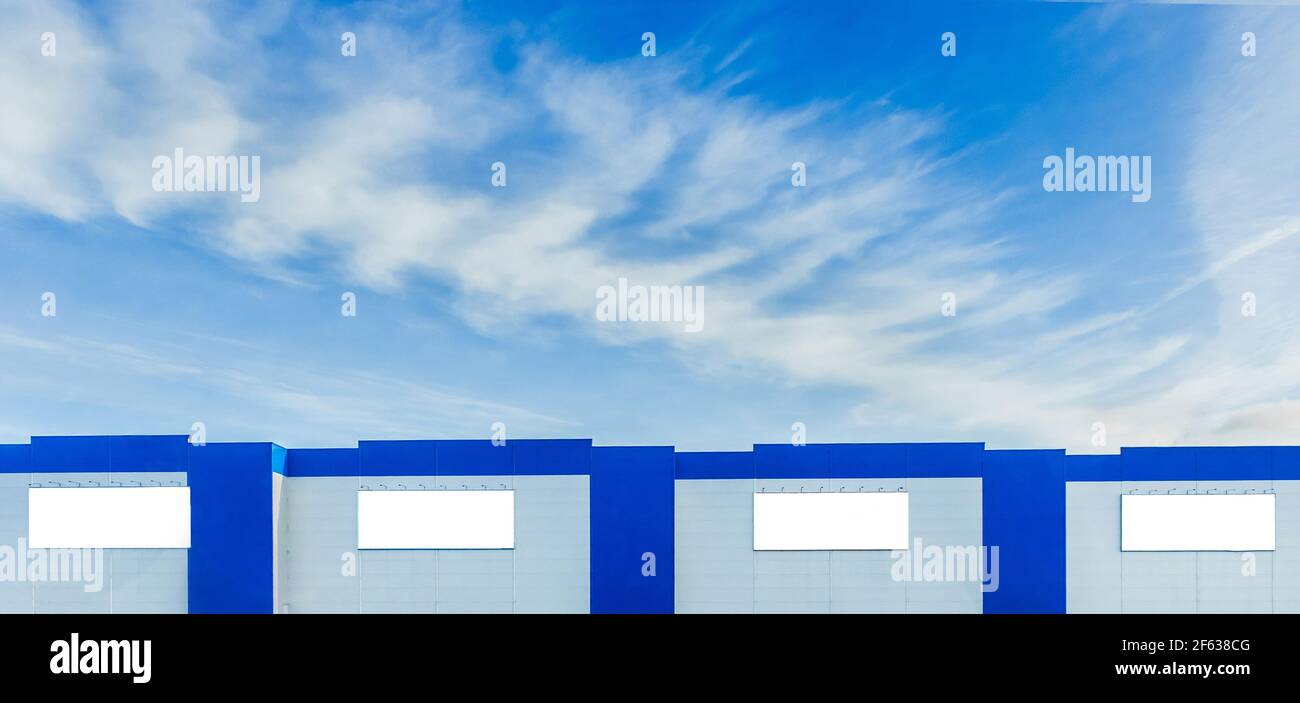 Mock up empty billboards on the modern facade of an urban building against a blue sky with clouds. Stock Photo