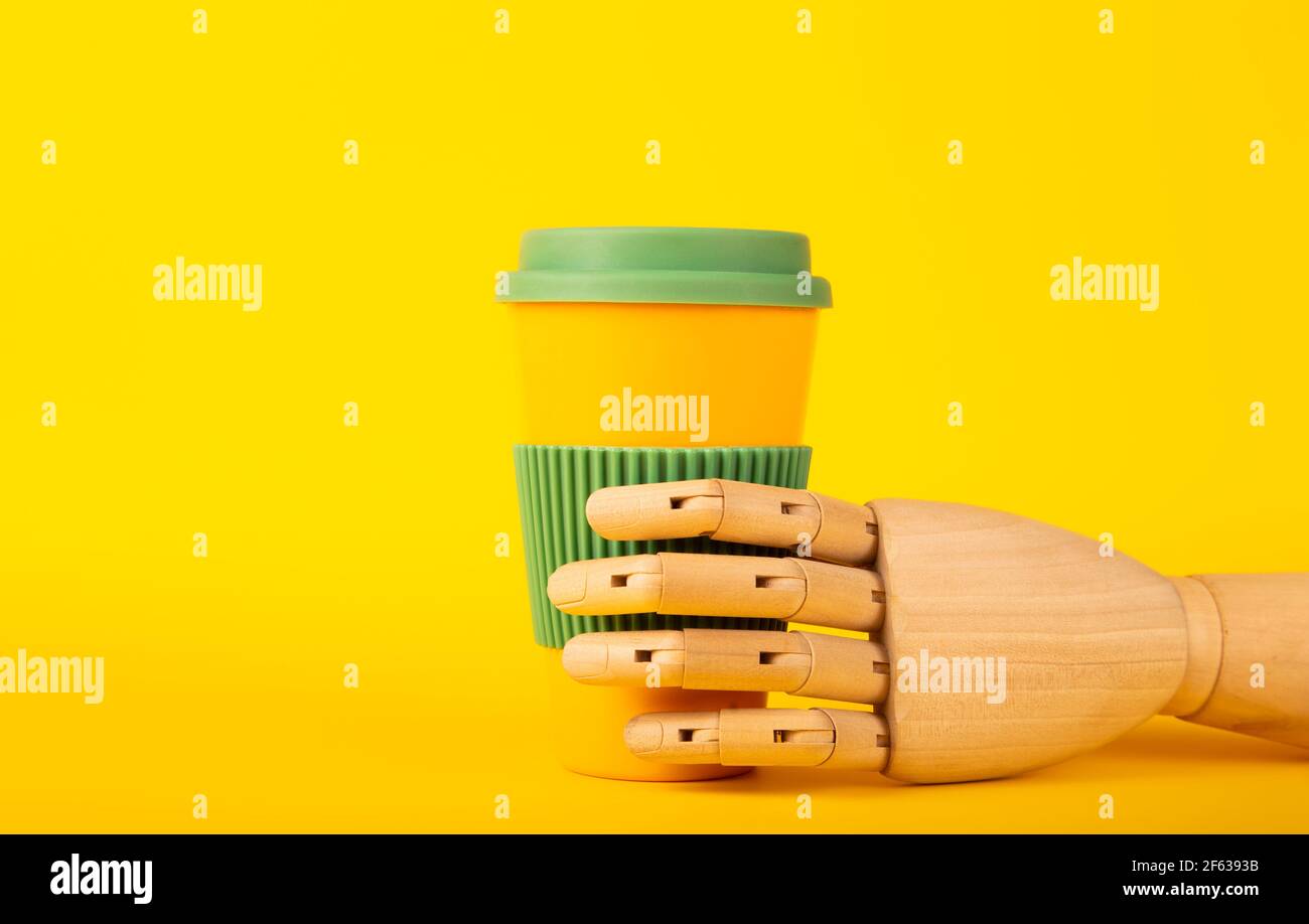 Wooden mannequin hand holding reusable coffee cup on a yellow background with space for text Stock Photo
