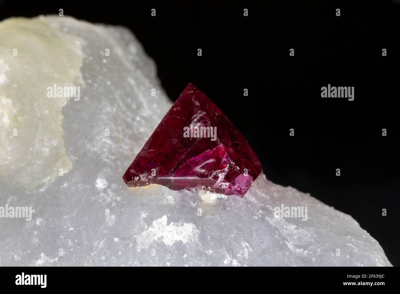 Red spinel crystal, uncut, still set in white host rock matrix. From Mogok region, Myanmar. Black background. Stock Photo
