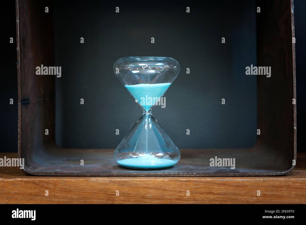 Blue sand running through a vintage glass hourglass measuring passing time in a concept of time management, deadline or countdown Stock Photo