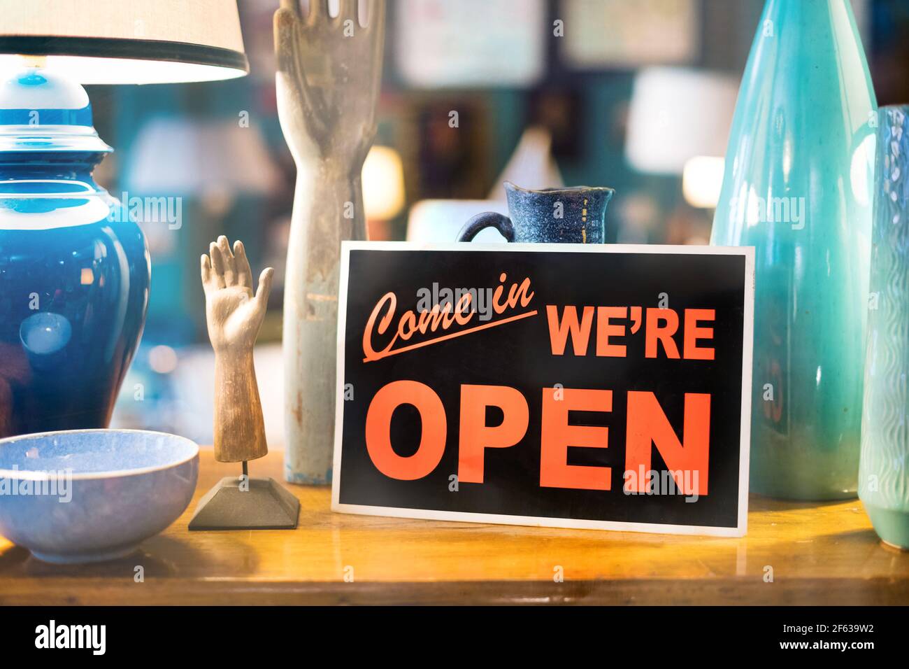 Come In We're Open for business or trading sign in a window of a shop or store propped against colorful handmade ceramics in close up Stock Photo