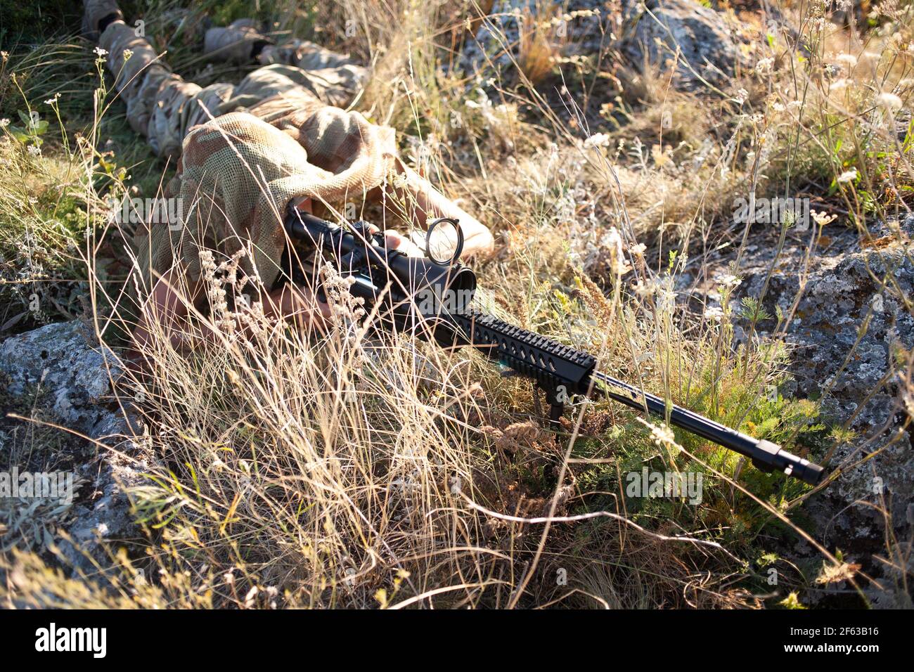 special operation forces sniper in ghillie (camouflage) suit with a high-precision rifle with optic scope in a combat position in the mountains Stock Photo