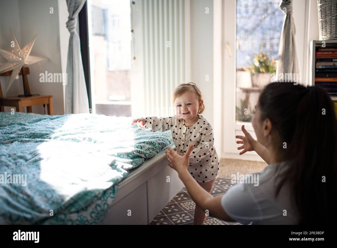 Small toddler girl with mother learning to walk in bedroom at home, first steps concept. Stock Photo