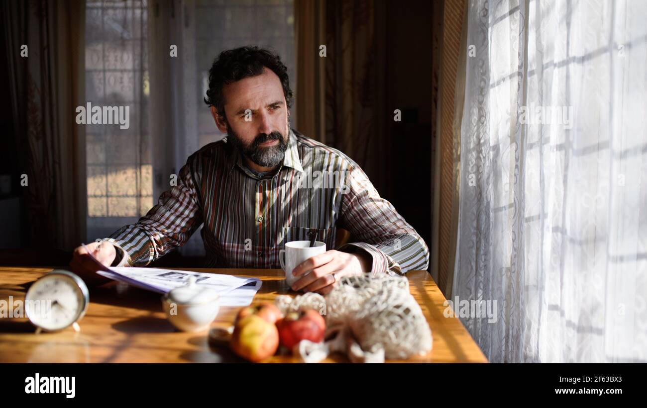 Portrait of unhappy poor mature man reading newspapers indoors at home, poverty concept. Stock Photo