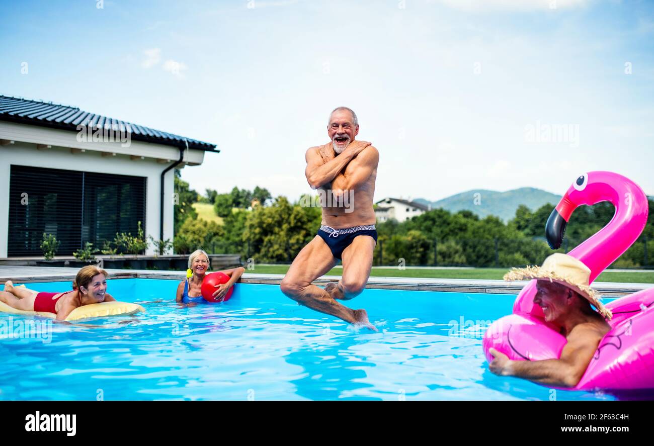 Group of cheerful seniors in swimming pool outdoors in backyard, jumping. Stock Photo