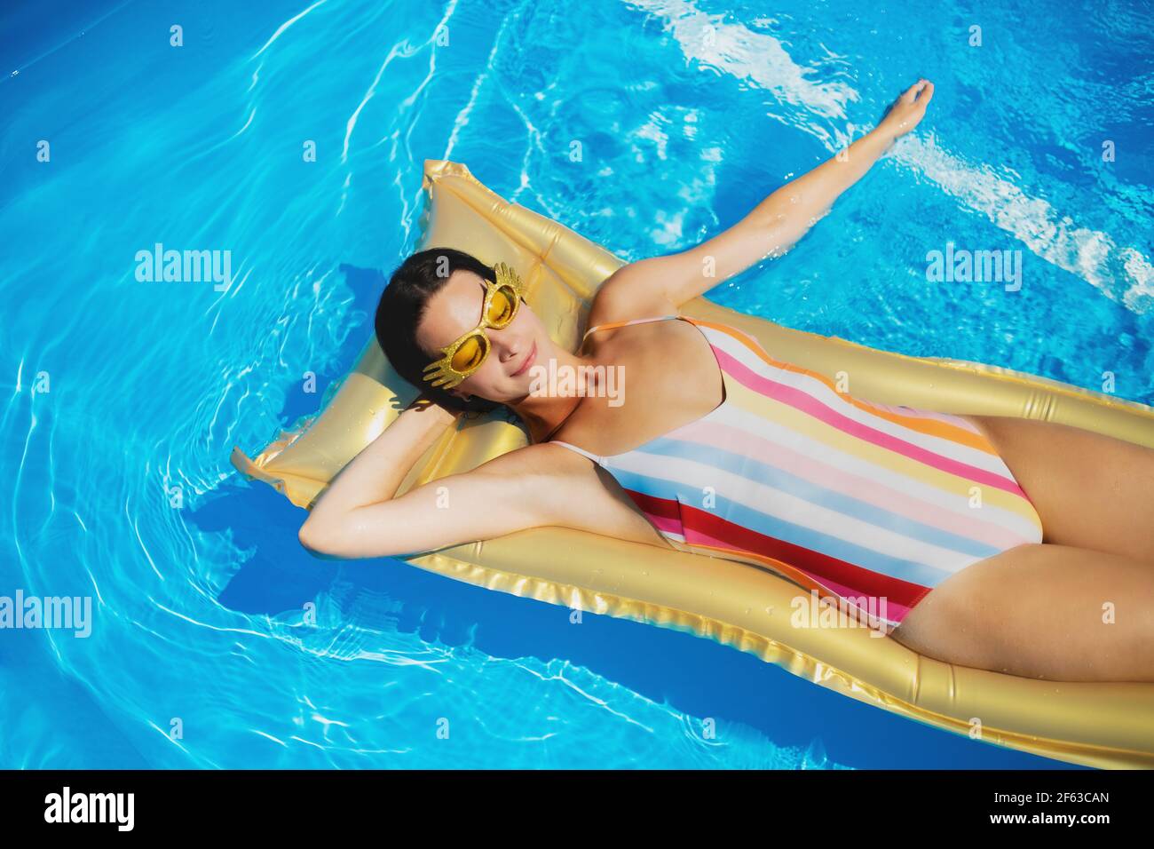 Top view of young woman in swimming pool outdoors on floating bed, relaxing. Stock Photo