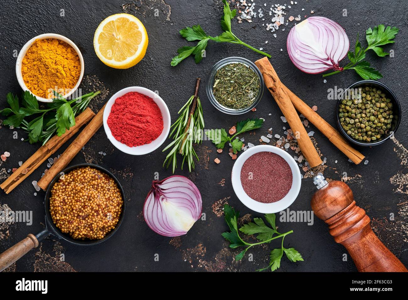 Set of Indian fragrant spices and herbs on a black stone background. Turmeric, dill, paprika, cinnamon, saffron, basil and rosemary in a spoon. Top vi Stock Photo