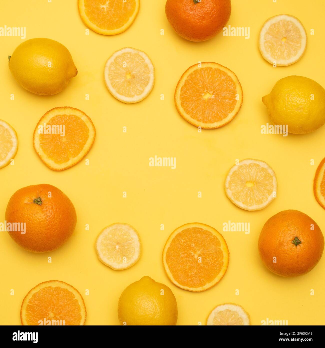 slices of oranges and lemons surrounding an empty space in a circular shape accompanied by whole oranges and lemons on a yellow background Stock Photo