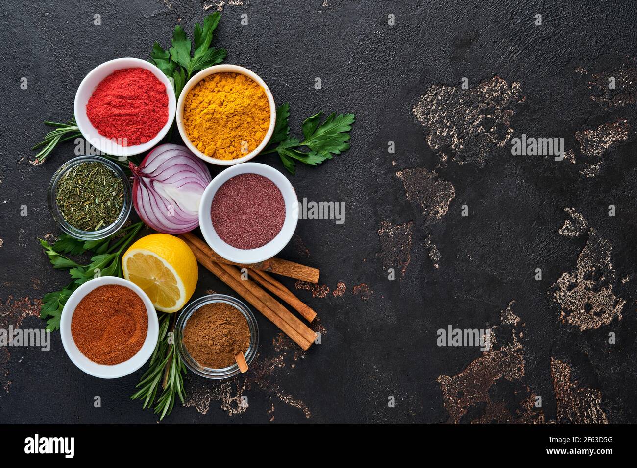 Set of Indian fragrant spices and herbs on a black stone background. Turmeric, dill, paprika, cinnamon, saffron, basil and rosemary in a spoon. Top vi Stock Photo