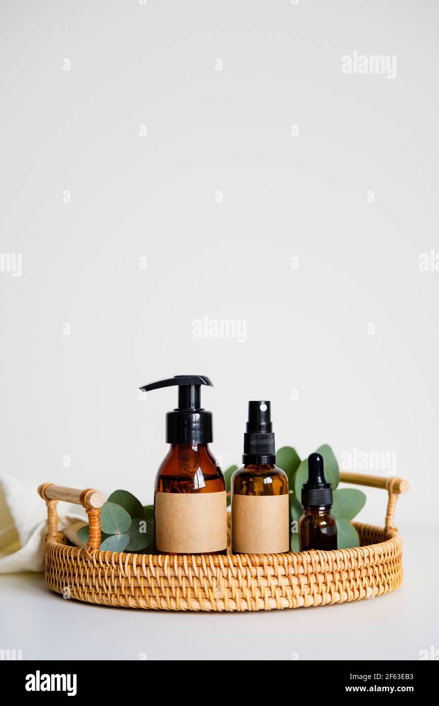 Amber glass cosmetic bottles in rattan tray with eucalyptus leaves and towel. Natural organic eco beauty products. Stock Photo
