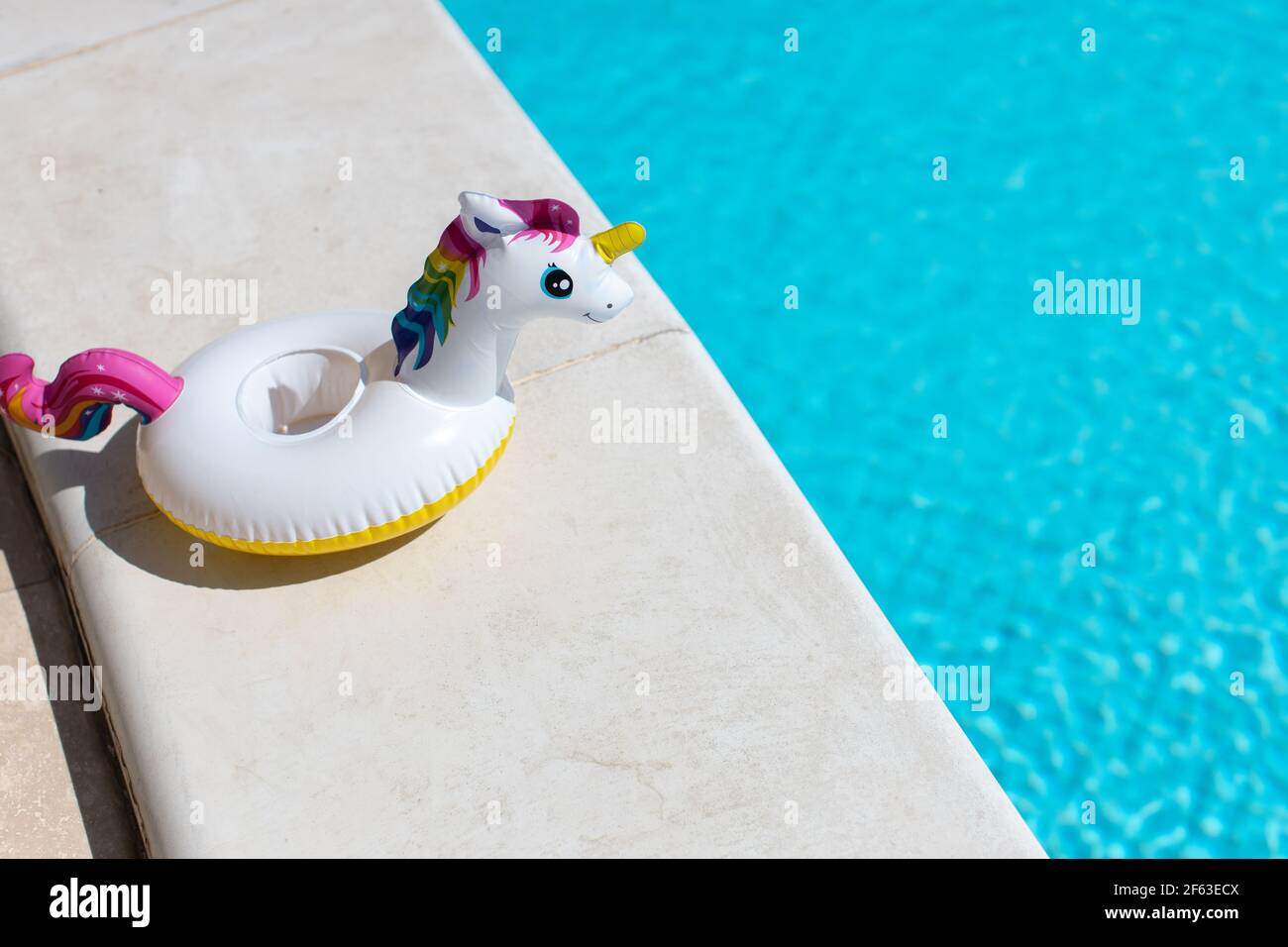 Inflatable pink mini rainbow unicorn, cocktail stand near swimming pool on bright sunny day, copy space. Concept summer vacation, entertainment, water Stock Photo