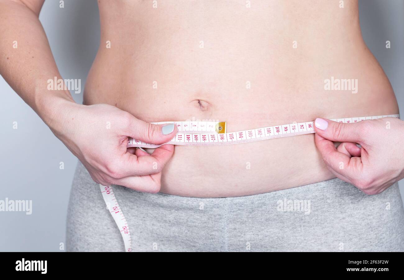 Overweight or fat adult woman is measureing around the body on the midriff on a gray background. Healthcare, medicine concept. Stock Photo